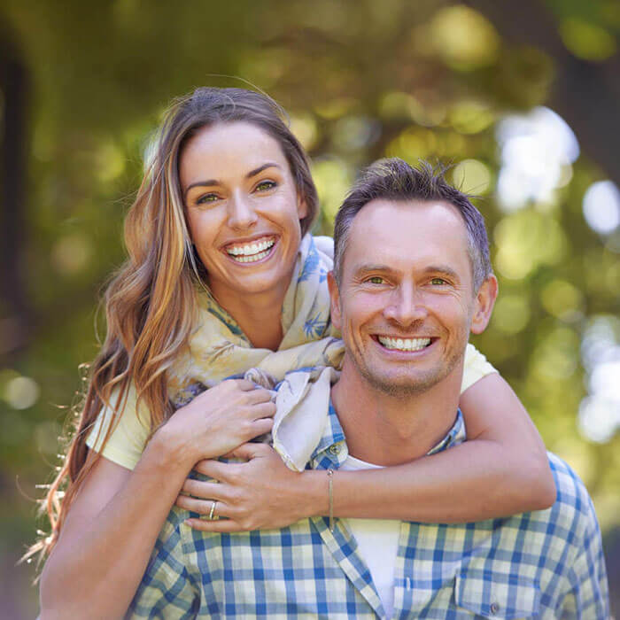 man smiling outdoors with woman hanging on his back