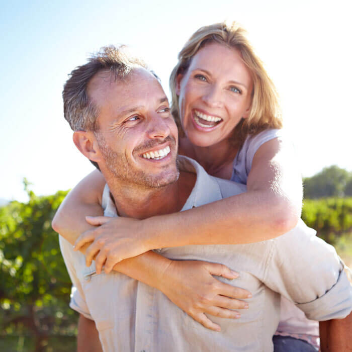 man smiling outdoors with woman hanging on his back