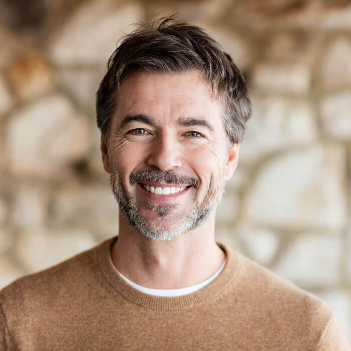 man smiling in front of stone wall